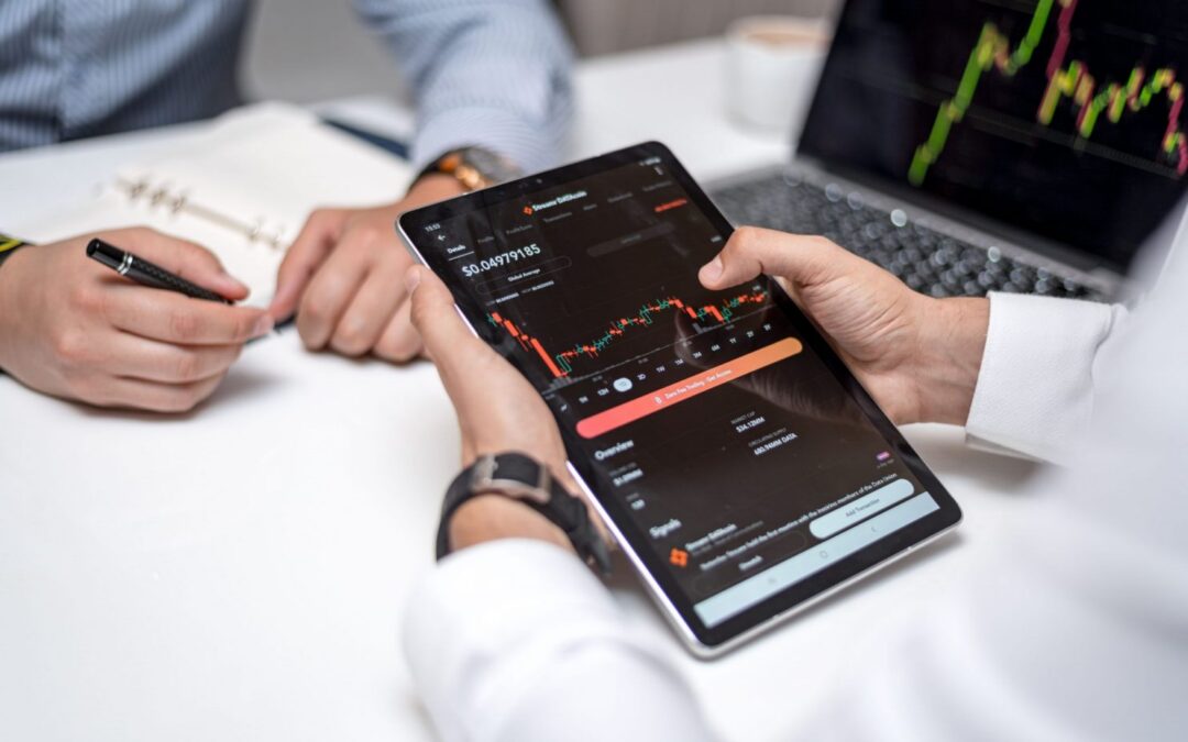 2 men sitting at a table analyzing fintech and investment data on a tablet.
