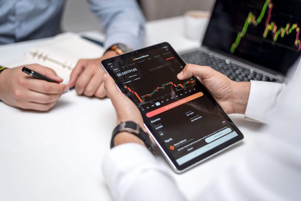 2 men sitting at a table analyzing fintech and investment data on a tablet.