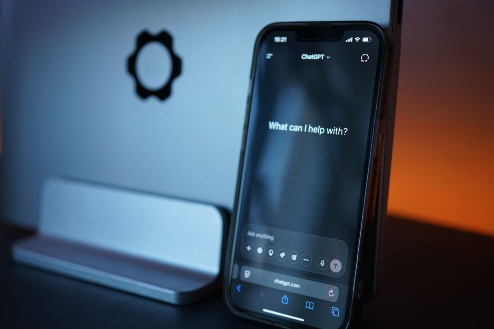 Image of a smartphone with an AI chat open and a computer in the background.