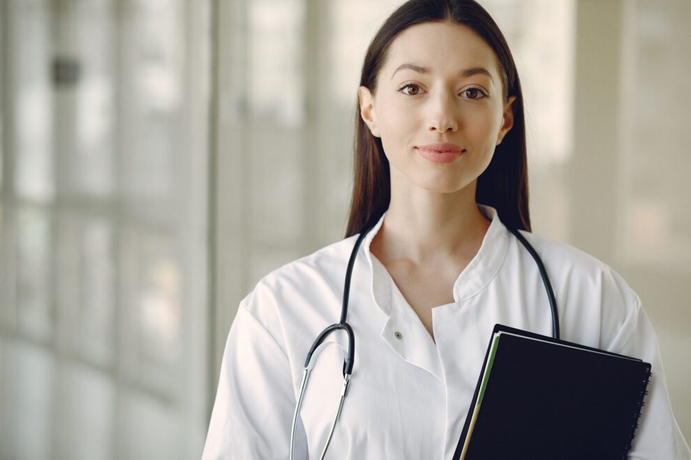 Female doctor in a white coat with stethoscope and notebook.